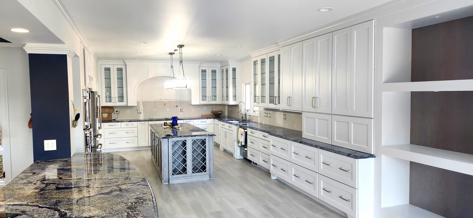 Contemporary kitchen remodel featuring white shaker cabinets, blue granite countertops, central island with wine rack, stainless steel appliances, and modern pendant lighting for a bright open-concept design.