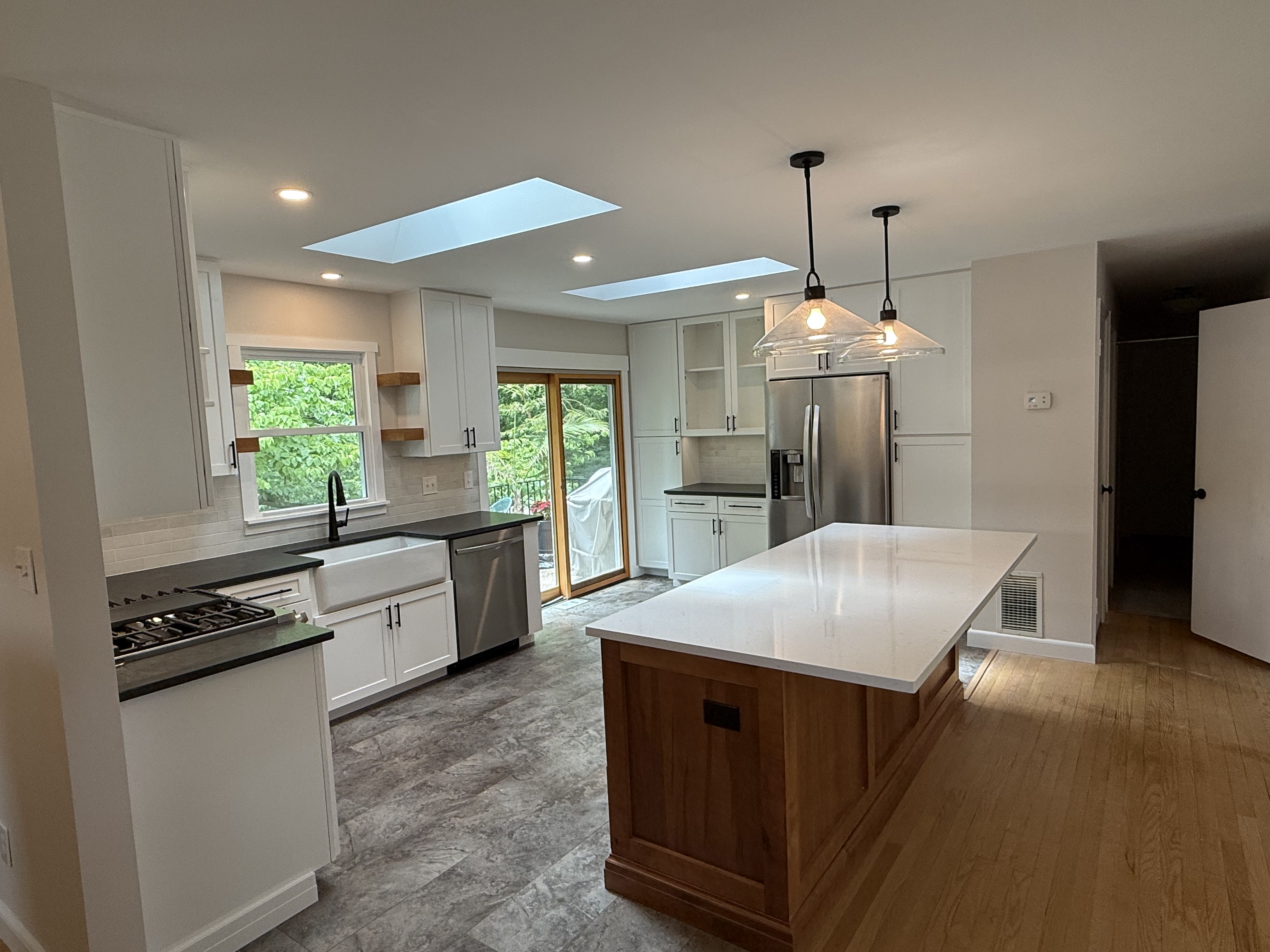Contemporary kitchen remodel featuring white shaker cabinets, natural wood island with quartz countertop, stainless steel appliances, farmhouse sink, pendant lighting, and skylights for bright natural illumination.