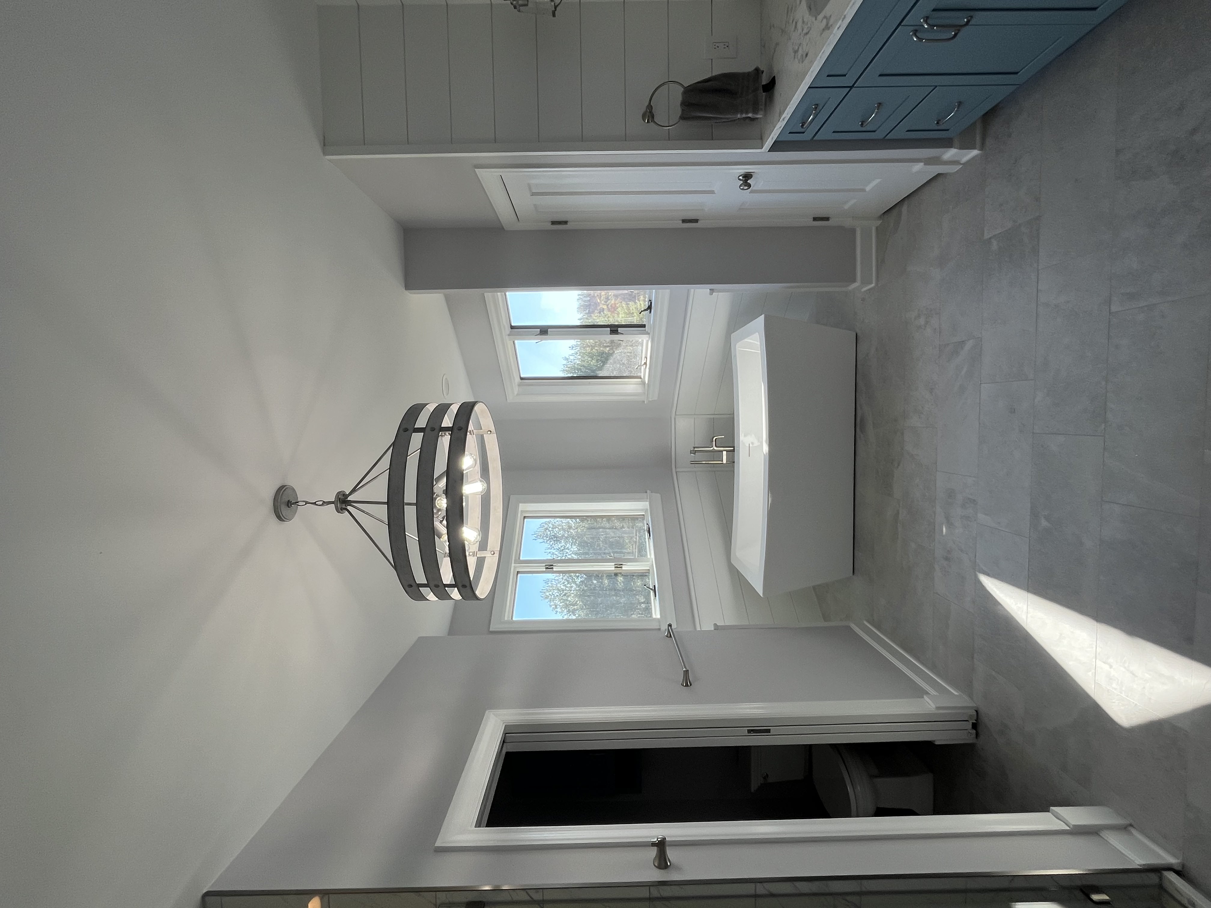 Luxury bathroom remodel featuring a modern freestanding soaking tub, blue vanity with marble countertop, shiplap accent wall, and large windows for natural light.