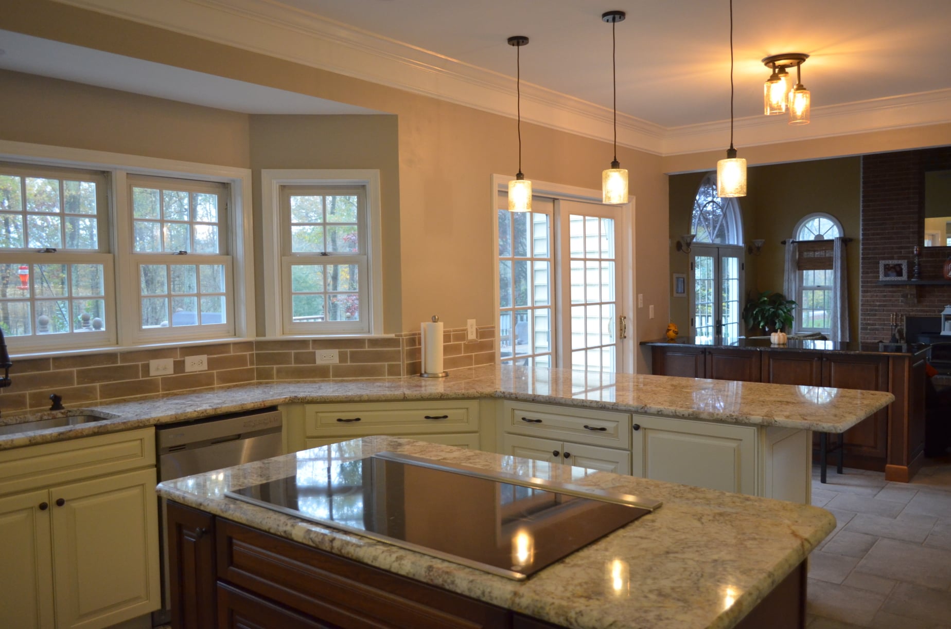Elegant kitchen remodel featuring granite countertops, cream cabinetry, stainless steel appliances, and pendant lighting over a large island with cooktop in an open-concept layout.